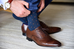 Men's navy blue dress socks with orange polka dots by Fit Elite displayed inside brown dress shoes
