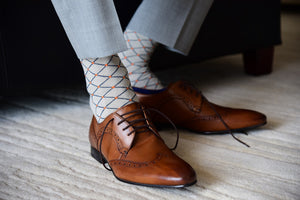 Men's patterned dress socks, grey with orange polka dots, displayed inside brown shoes