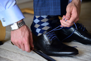 Argyle patterned dress socks for men matching blue dress pants, cufflinks, and a square watch